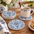 Blue and white floral ceramic coasters and a matching mug on a wooden table, styled with a striped napkin, flowers, and a scone.