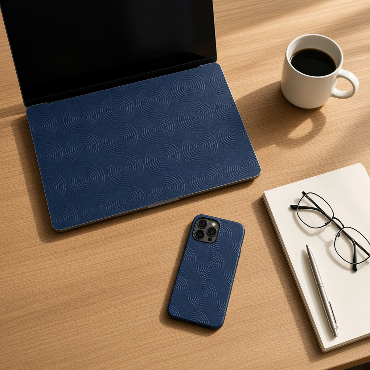 Laptop skin and phone case in navy subtle concentric rings on an oak desk, top-down, made with prompt #85