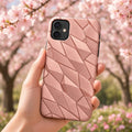 Hand holding a phone in a rose-gold titanium-like facets case under blossom trees, made with prompt #85