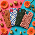 Four colourful relief phone cases (terracotta lotus, blue and white floral ceramic, green woven leather, rose-gold ripples) on a coral and turquoise backdrop, made with prompts #556, #477, #53 and #864