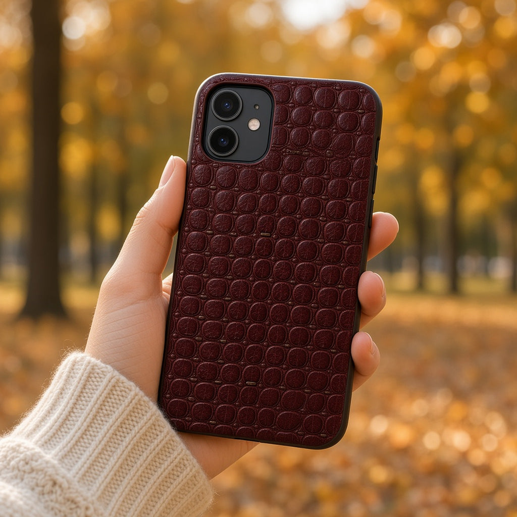Hand holding a phone in a burgundy leather crocodile-scale relief case in an autumn park, made with prompt #5