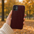 Hand holding a phone in a burgundy leather crocodile-scale relief case in an autumn park, made with prompt #5