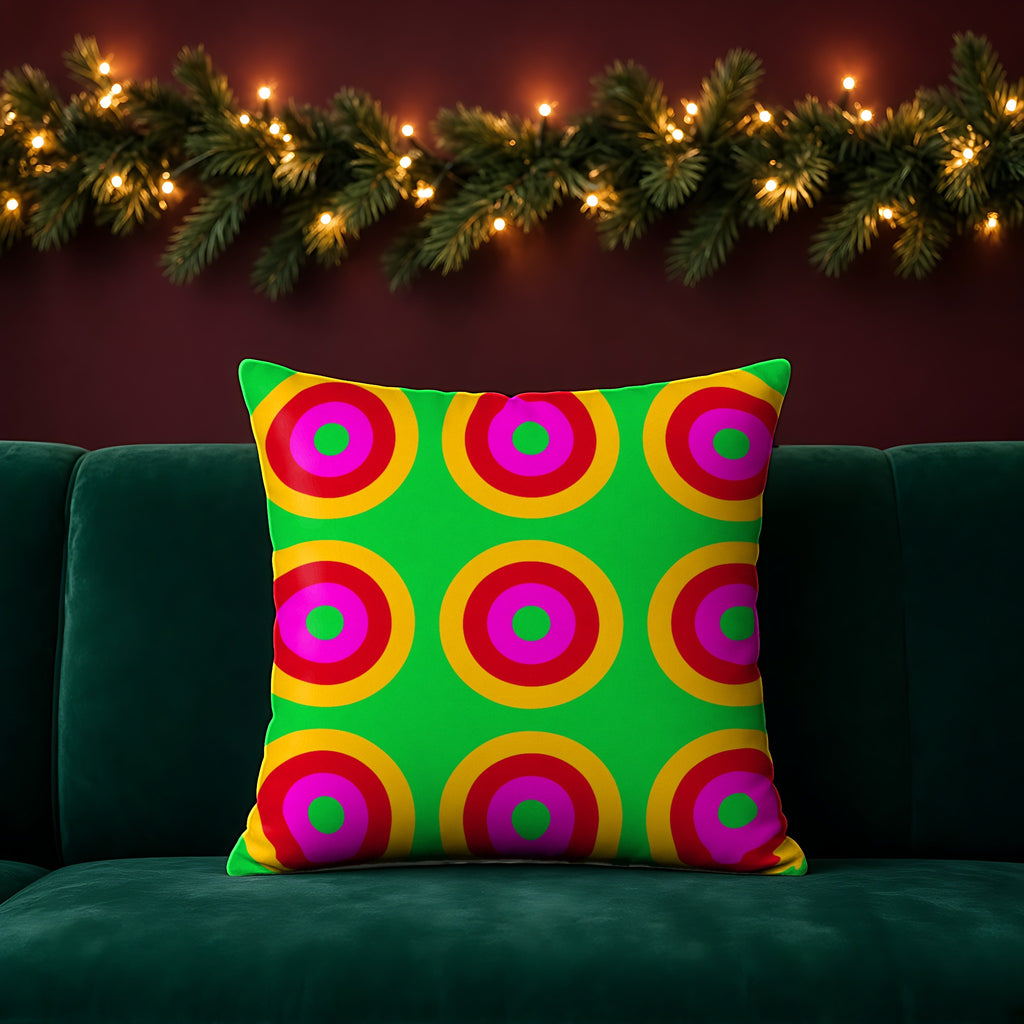 Giant Op-Art Jewel Rings faux suede cushion in the Christmas Jewel Bright palette, on an emerald sofa in a festive room with a garland and fairy lights
