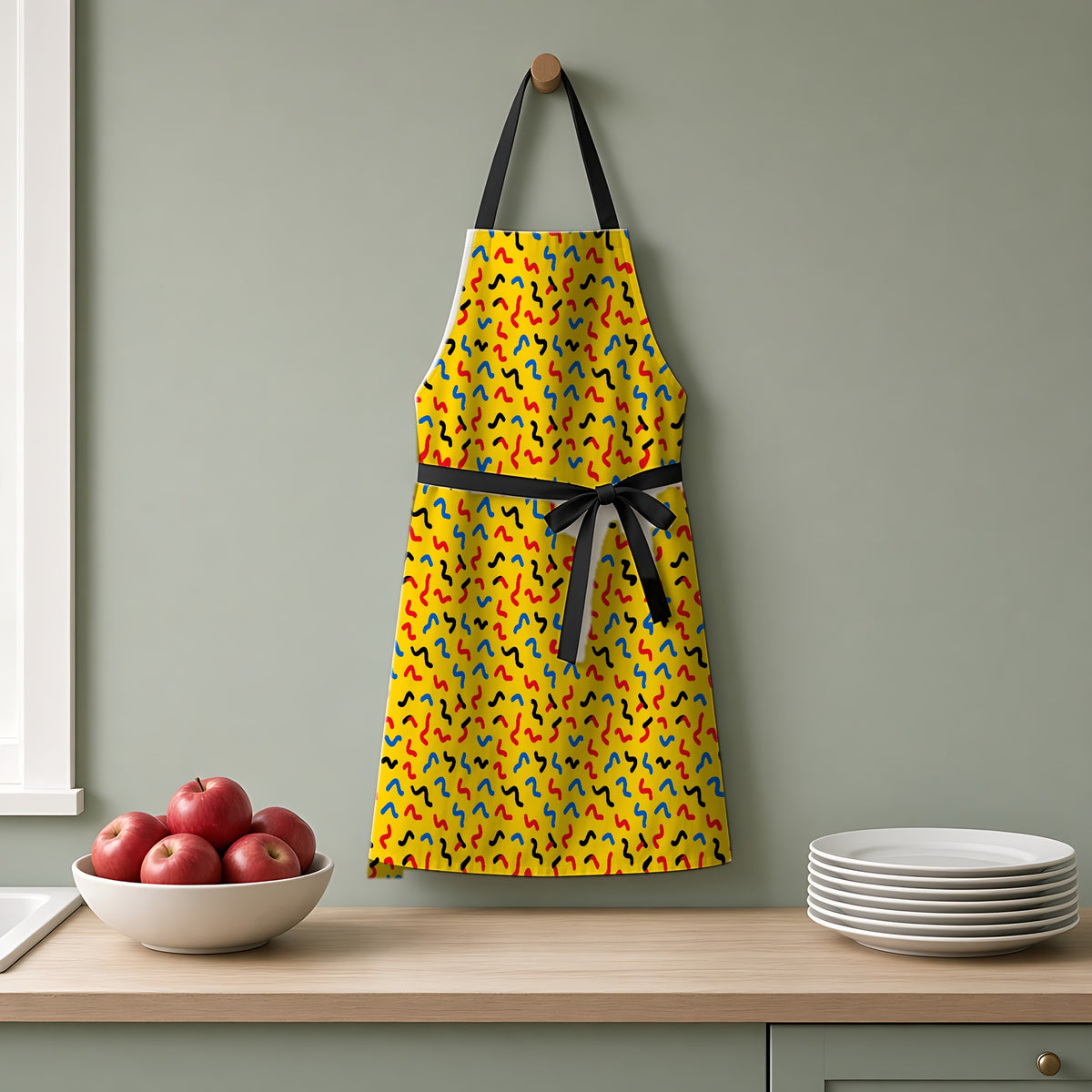 Squiggle Strokes Yellow Apron hanging on a sage-green kitchen wall
