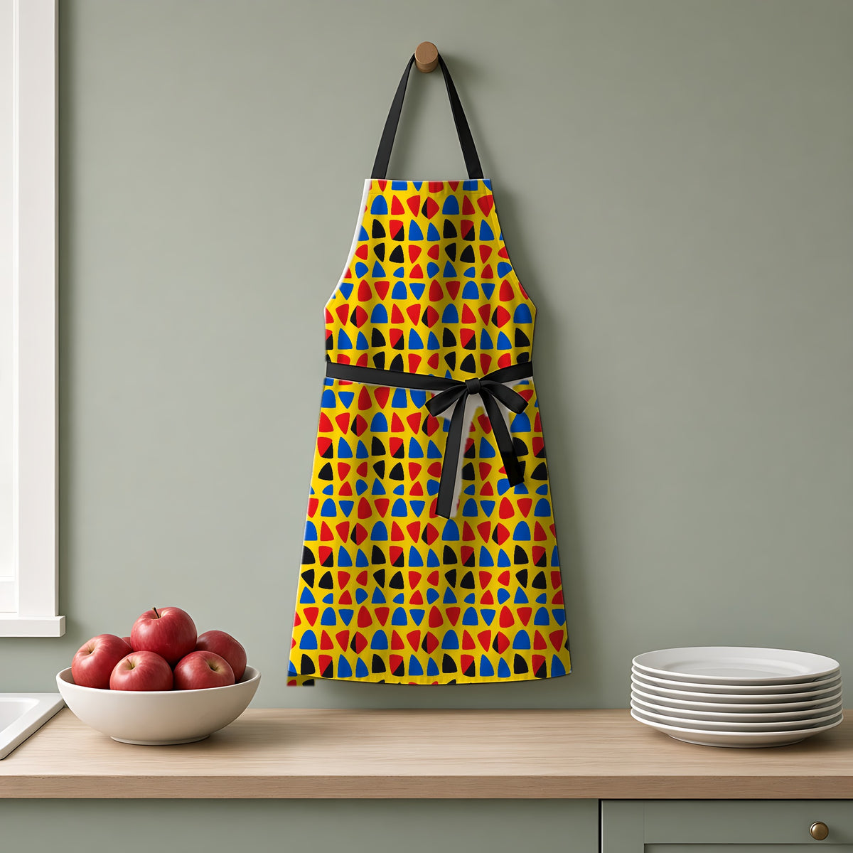 Cut-Out Arcs Yellow Apron hanging on a sage-green kitchen wall
