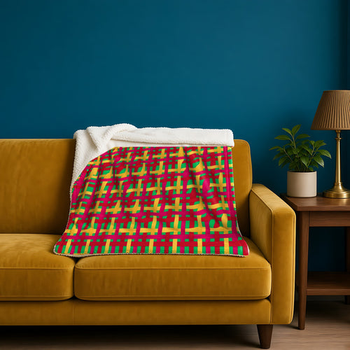 Big Jewel Ribbon Weave sherpa fleece blanket in the Christmas Jewel Bright palette, draped over a mustard sofa against a deep-teal wall
