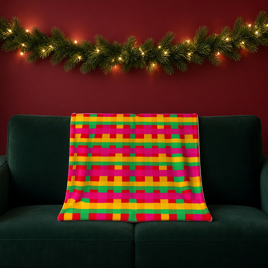 Grand Jewel Plaid sherpa fleece blanket in the Christmas Jewel Bright palette, draped over a green sofa in a festive room with a garland and fairy lights