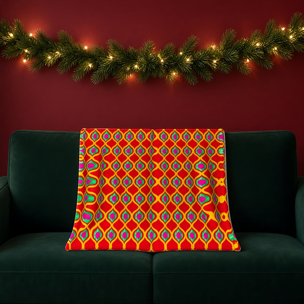 Grand Gold Ogee Lattice II sherpa fleece blanket in the Christmas Jewel Bright palette, draped over a green sofa in a festive room with a garland and fairy lights