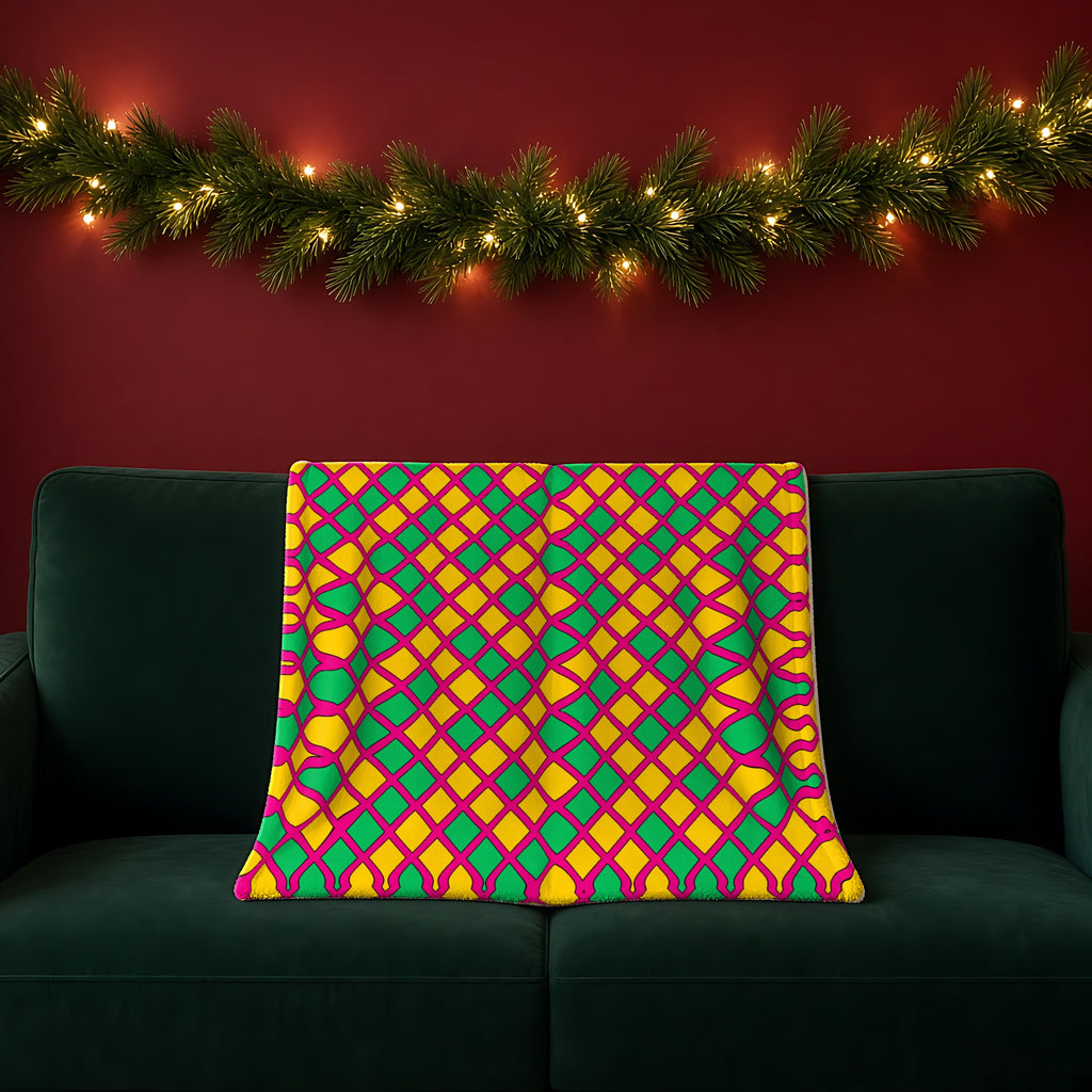 Harlequin Gold Grid sherpa fleece blanket in the Festive Jewel Bright palette, draped over a green sofa in a festive room with a garland and fairy lights