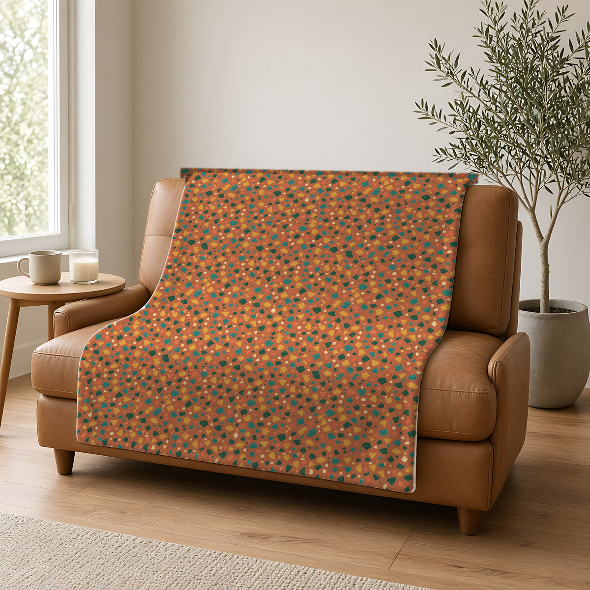 Jewel Chip Terrazzo Sherpa Fleece Blanket draped over a caramel leather sofa