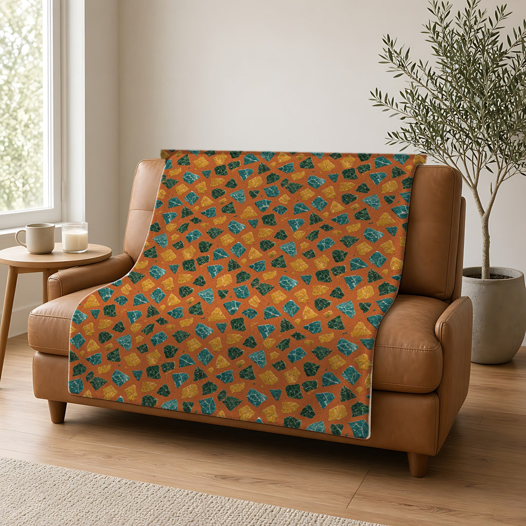 Marble Fragment Toss Sherpa Fleece Blanket draped over a caramel leather sofa