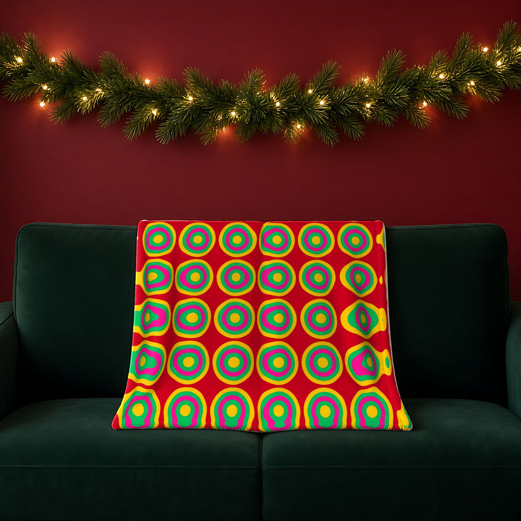 Mega Ring Grid sherpa fleece blanket in the Festive Jewel Bright palette, draped over a green sofa in a festive room with a garland and fairy lights