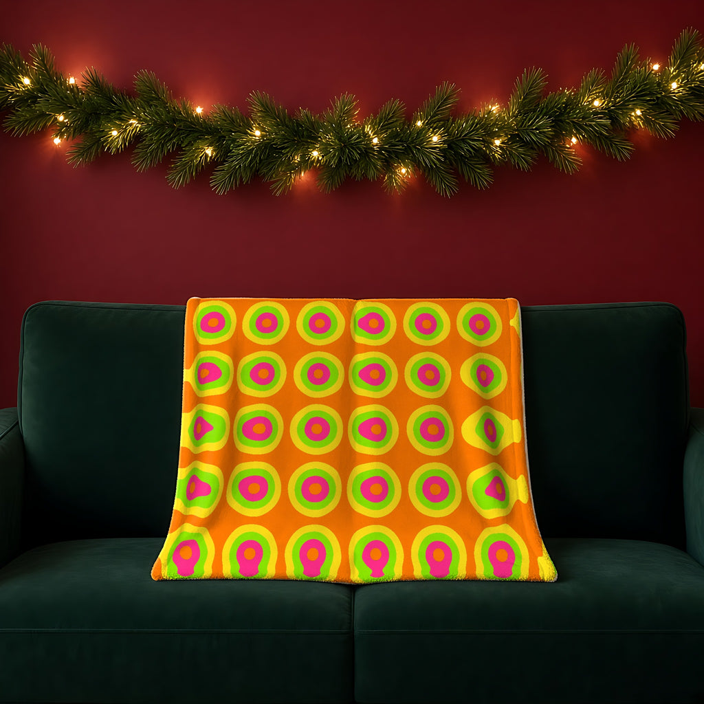 Giant Op-Art Jewel Rings Sherpa Fleece Blanket in the Hot Citrus Festive palette, draped over a green sofa in a festive room with a garland and fairy lights