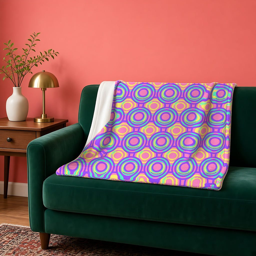Interlocking Ring Ripples Sherpa Fleece Blanket in the Candy Pastel on Grape palette, draped over a green sofa against a coral wall