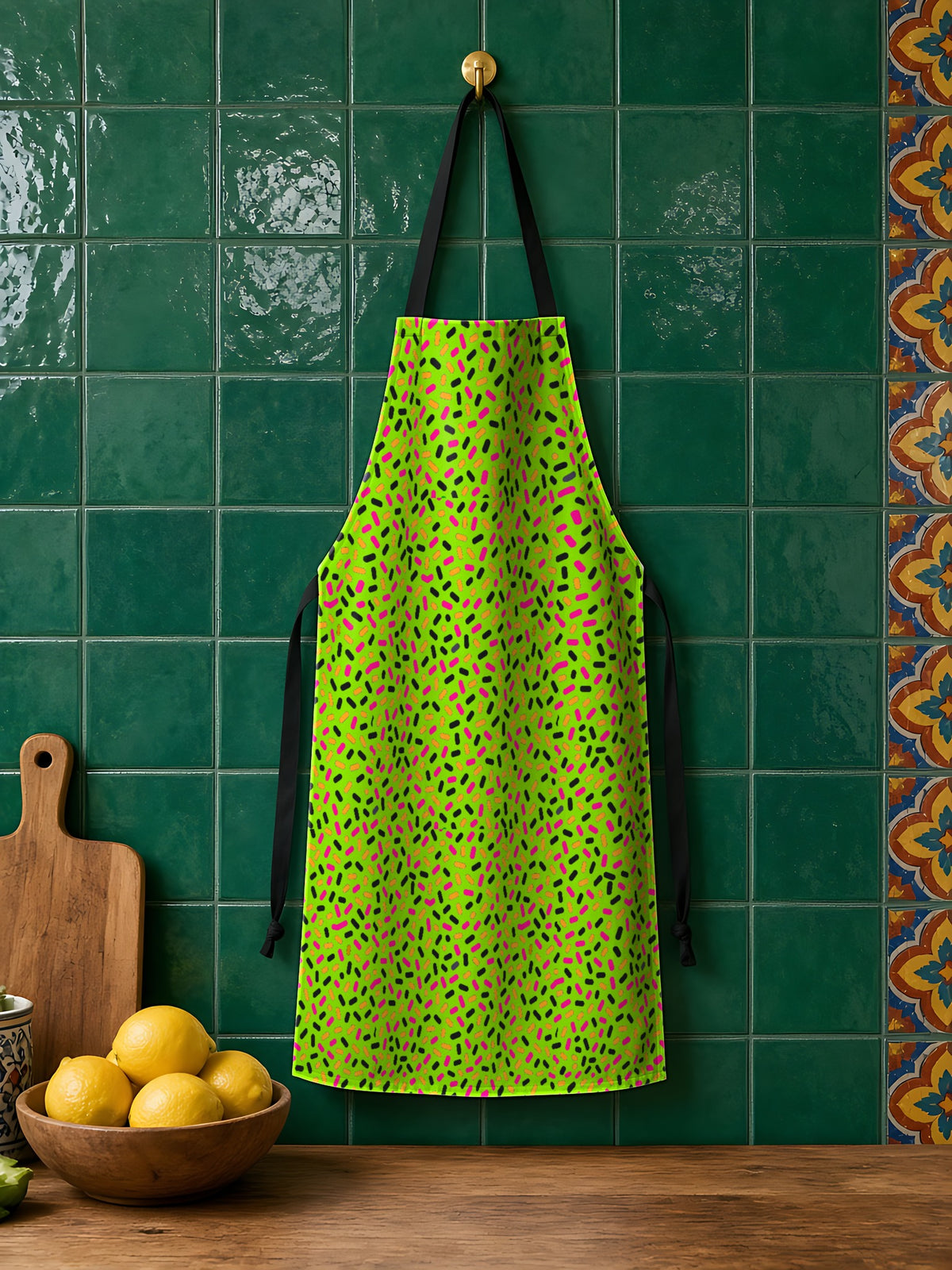 Sprinkle Pop Apron in the Tropical Punch palette, hanging against an emerald-tiled kitchen wall