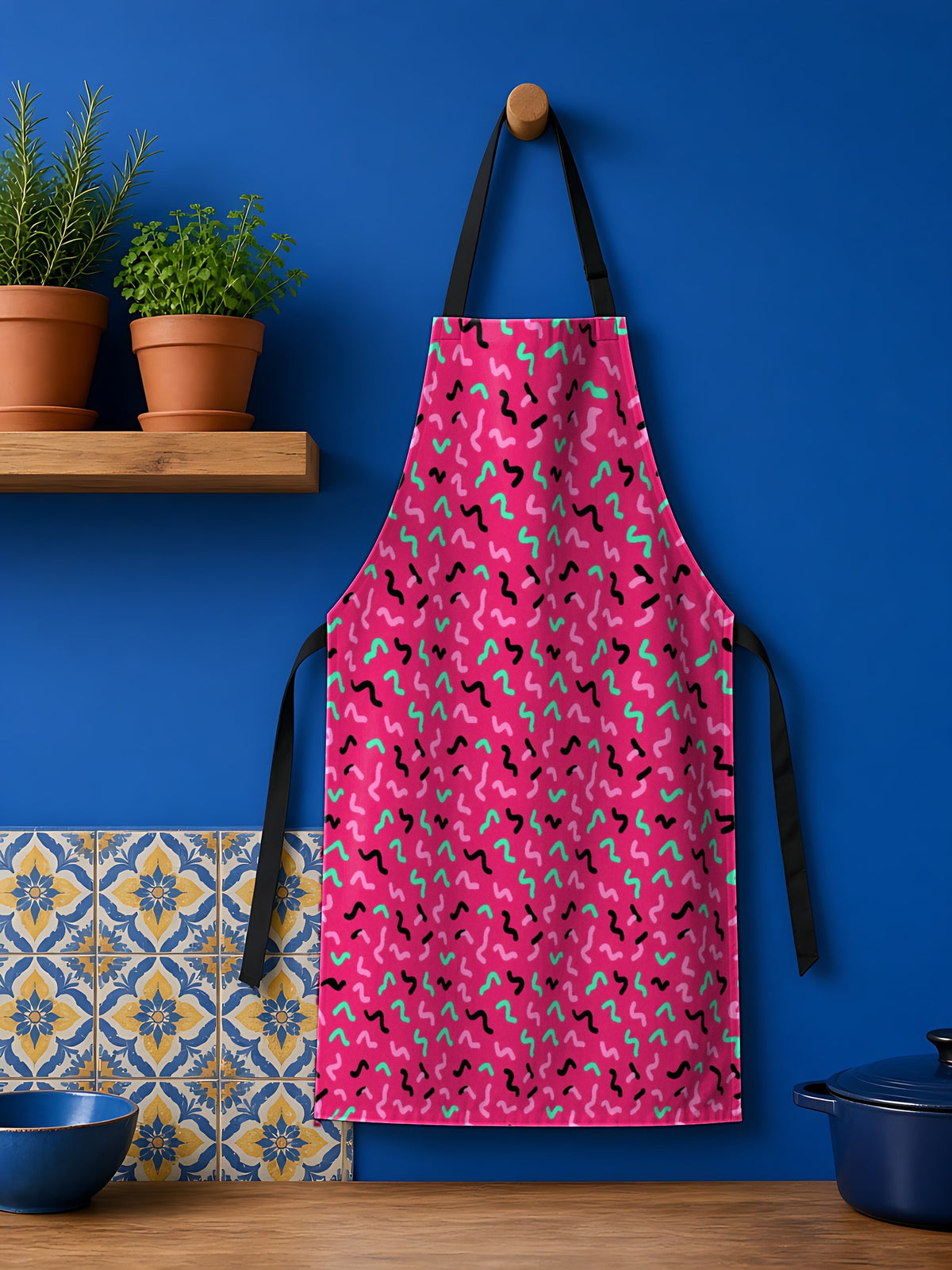 Squiggle Strokes Apron in the Candy Pop on Raspberry palette, hanging against a cobalt-blue kitchen wall