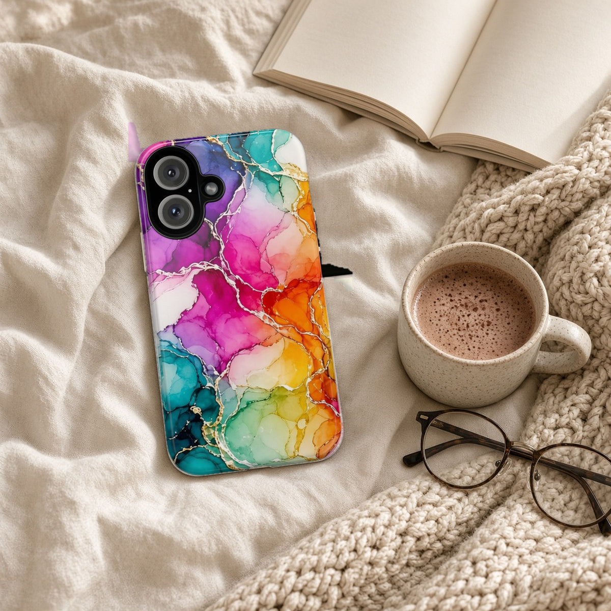 Rainbow Alcohol Ink Bloom tough phone case on a cosy knit blanket with a hot chocolate and glasses
