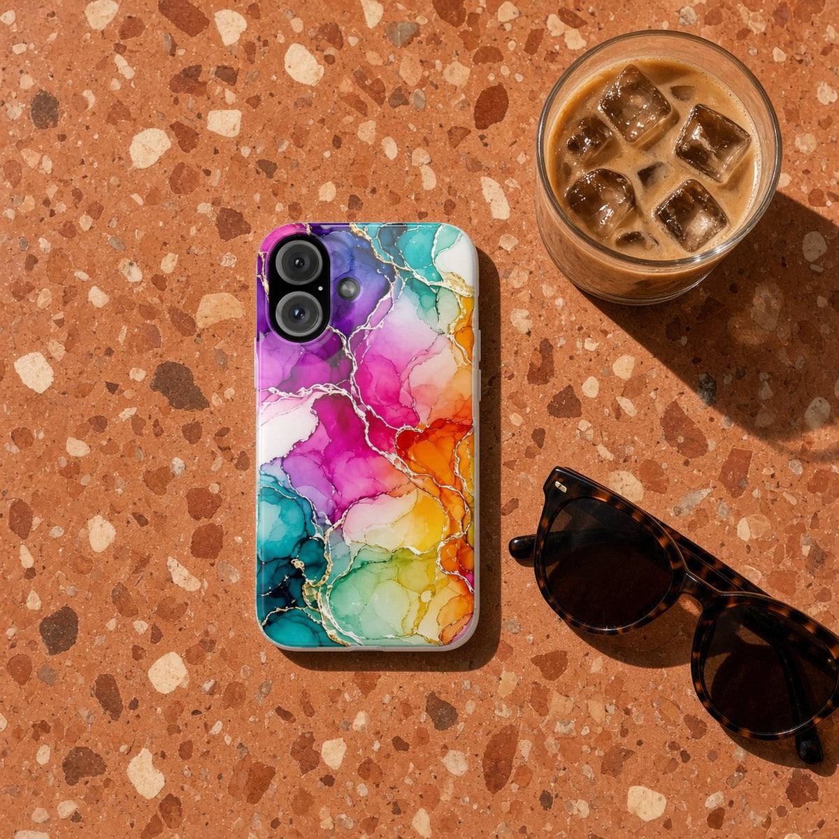 Rainbow Alcohol Ink Bloom slim phone case on terrazzo with an iced coffee and sunglasses