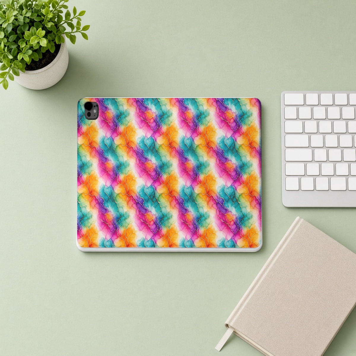 Rainbow Alcohol Ink Bloom iPad folio case from above on a sage desk with a keyboard and notebook