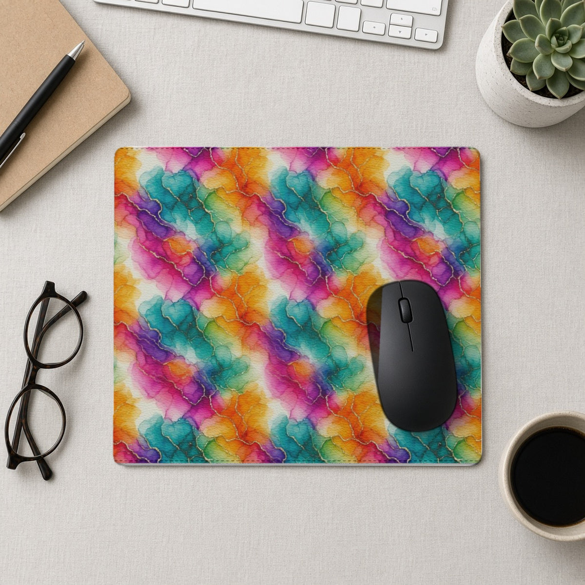 Rainbow Alcohol Ink Bloom vegan leather mouse mat from above with a mouse, notebook and glasses