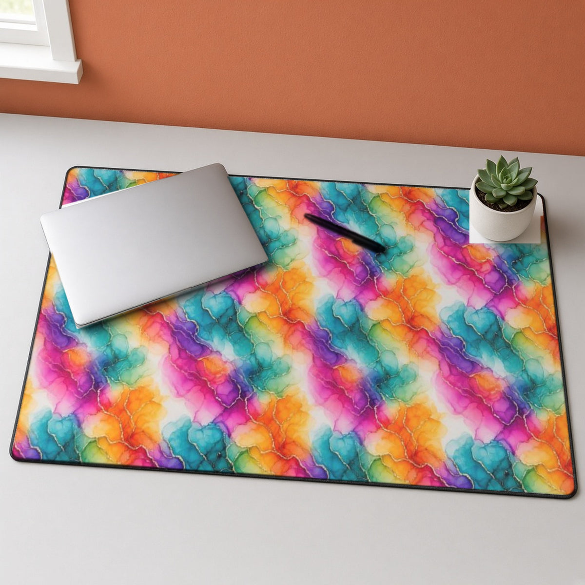 Rainbow Alcohol Ink Bloom desk mat on a grey desk with a laptop and a plant