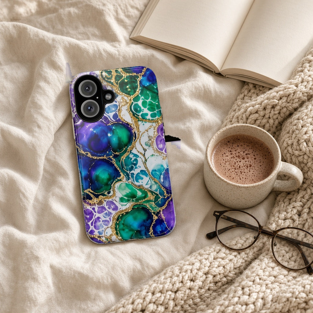 Peacock Acrylic Pour Cells tough phone case on a cosy knit blanket with a hot chocolate and glasses