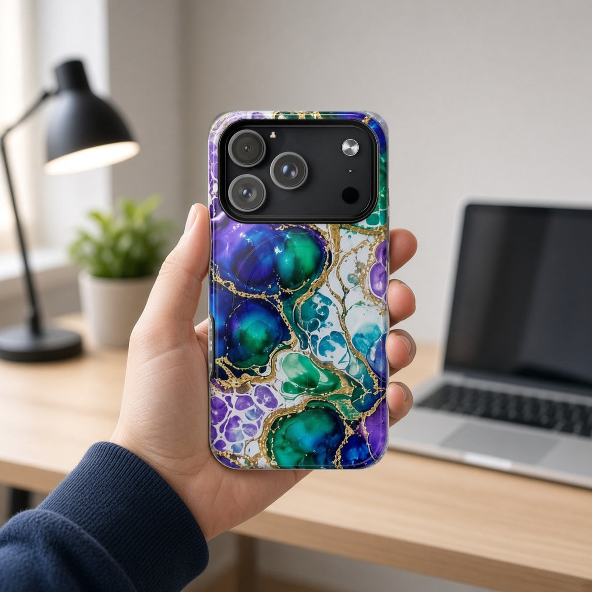 Hand holding the Peacock Acrylic Pour Cells magnetic iPhone case at a home office desk