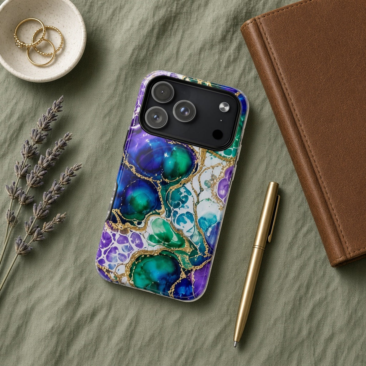 Peacock Acrylic Pour Cells magnetic iPhone case flat lay on sage linen with a notebook and pen