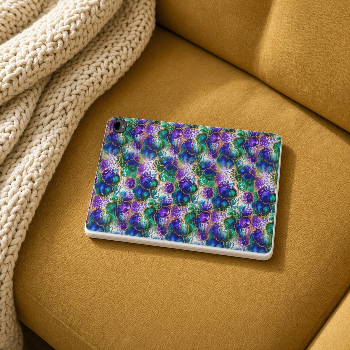 Peacock Acrylic Pour Cells iPad folio case on a mustard sofa with a knit throw