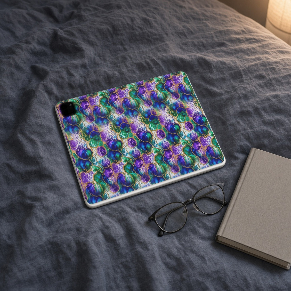 Peacock Acrylic Pour Cells iPad folio case on slate-blue bedding with a book and glasses