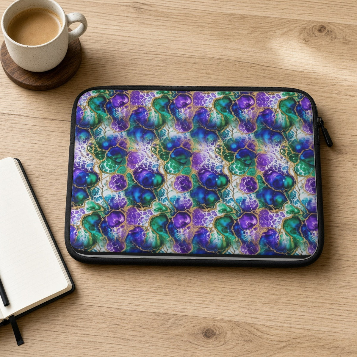 Peacock Acrylic Pour Cells laptop sleeve on an oak desk with coffee and a notebook