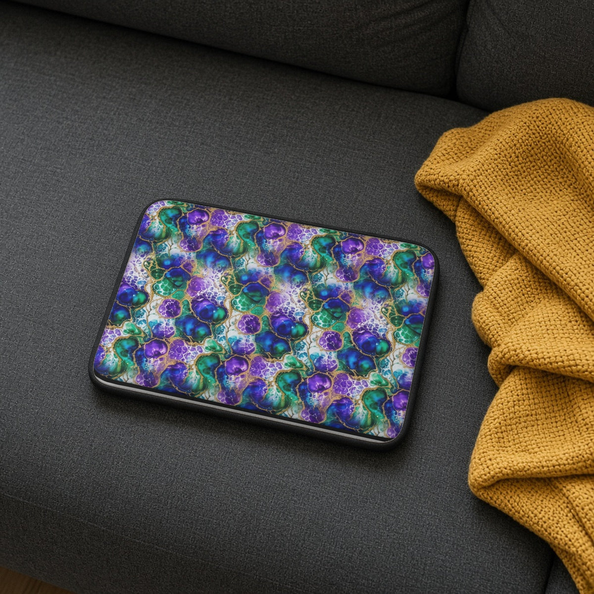 Peacock Acrylic Pour Cells laptop sleeve on a charcoal sofa with a cosy throw