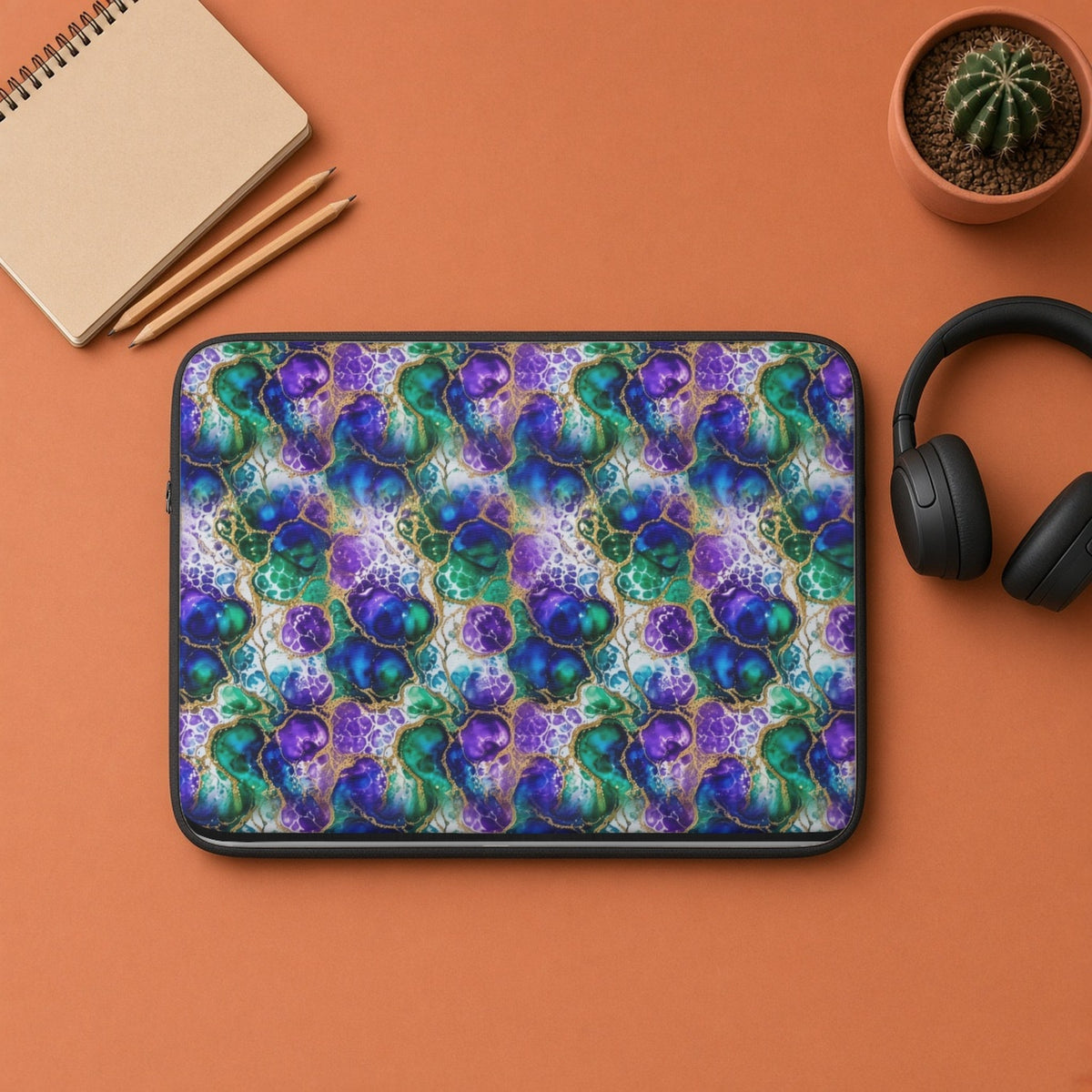 Peacock Acrylic Pour Cells laptop sleeve flat lay on terracotta with headphones and a notebook