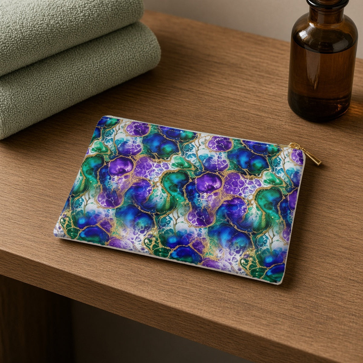 Peacock Acrylic Pour Cells zip accessory pouch on a wooden shelf with towels and an amber bottle