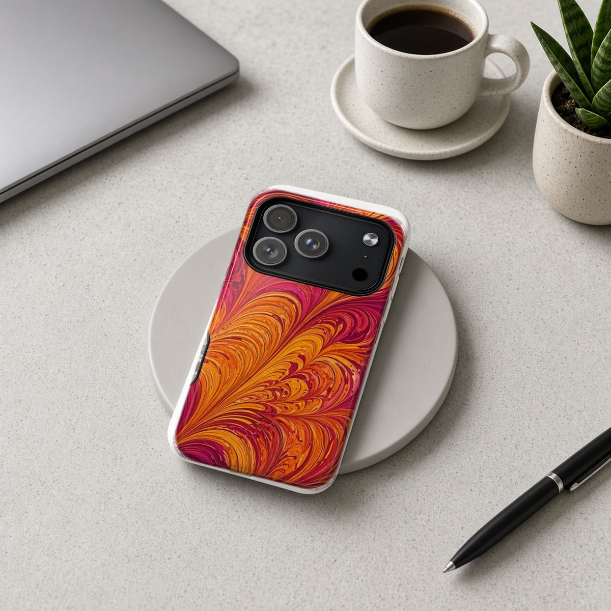Sunset Feather Marbling magnetic iPhone case on a wireless charging pad on a grey desk