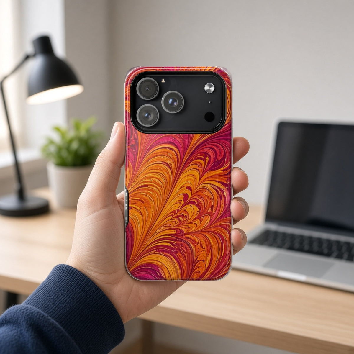 Hand holding the Sunset Feather Marbling magnetic iPhone case at a home office desk