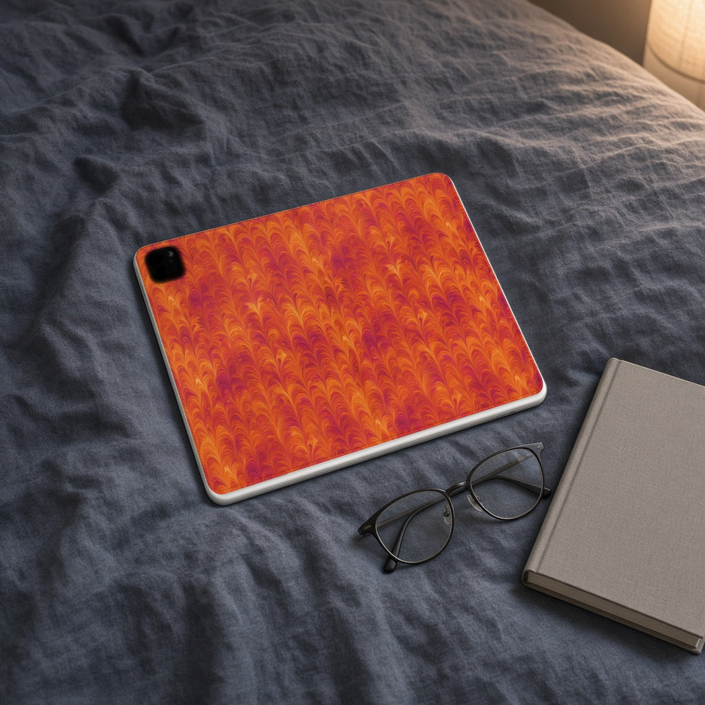 Sunset Feather Marbling iPad folio case on slate-blue bedding with a book and glasses