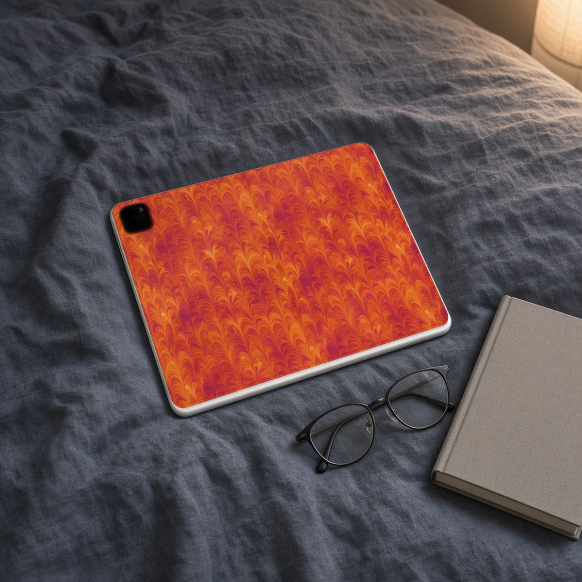 Sunset Feather Marbling iPad folio case on slate-blue bedding with a book and glasses