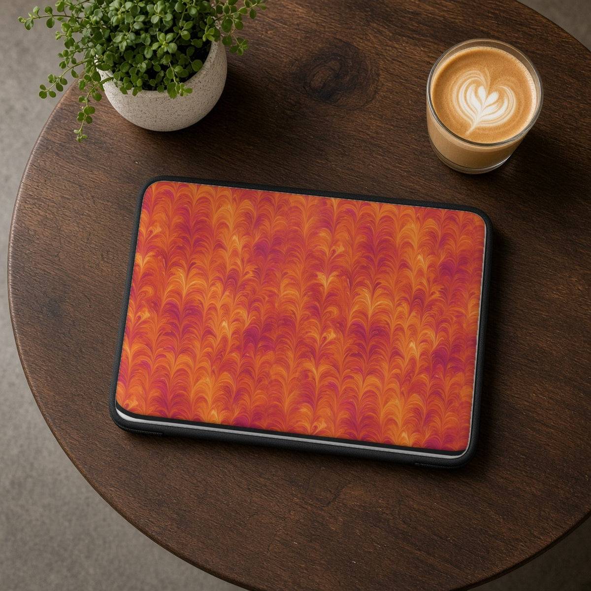 Sunset Feather Marbling laptop sleeve on a round wooden cafe table with a latte