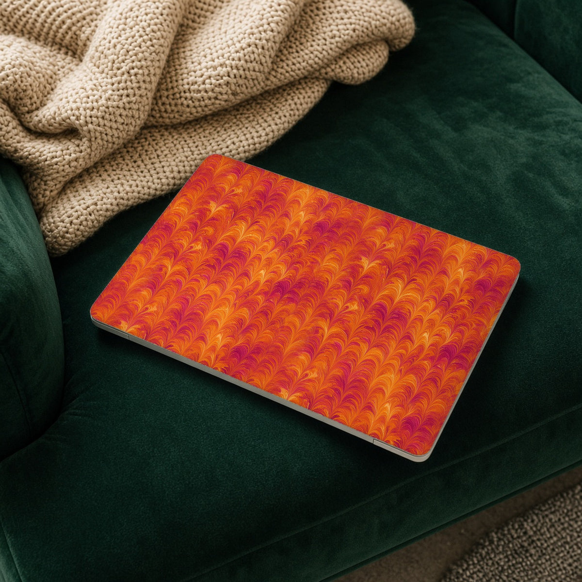 Sunset Feather Marbling matte MacBook case on a laptop resting on a green velvet sofa