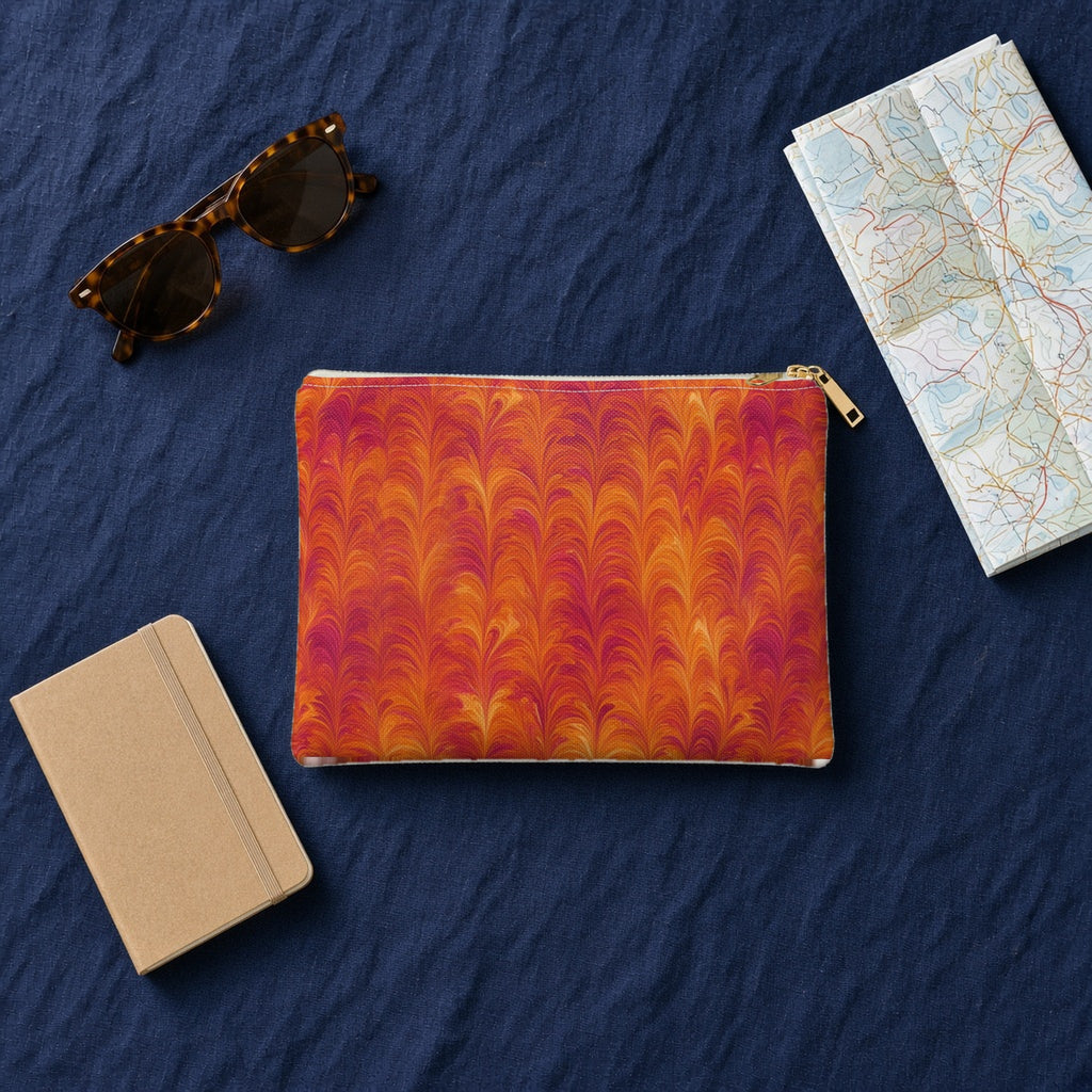 Sunset Feather Marbling zip accessory pouch on navy linen with sunglasses, a notebook and map
