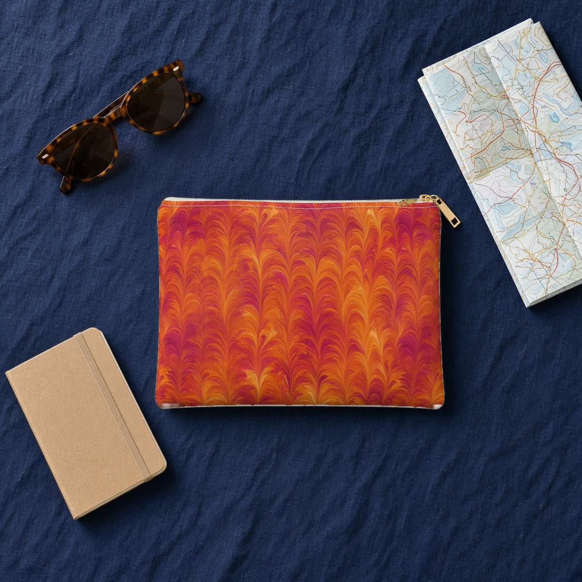 Sunset Feather Marbling zip accessory pouch on navy linen with sunglasses, a notebook and map