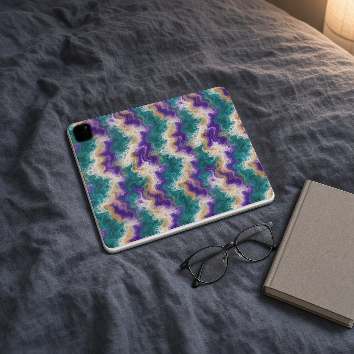Peacock Resin Wave iPad folio case on slate-blue bedding with a book and glasses