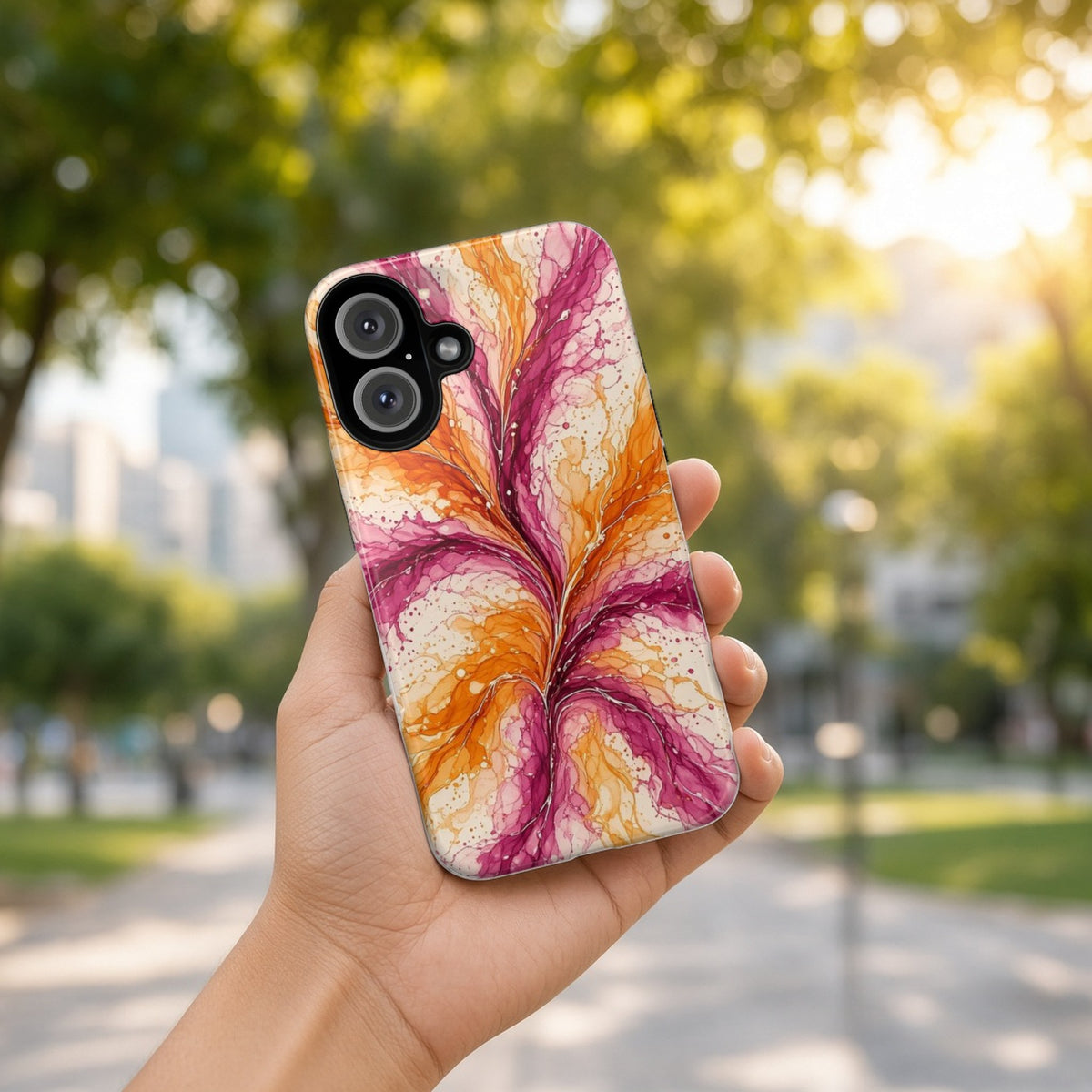 Hand holding the Sunset Ink Branches tough phone case outdoors in a sunny park