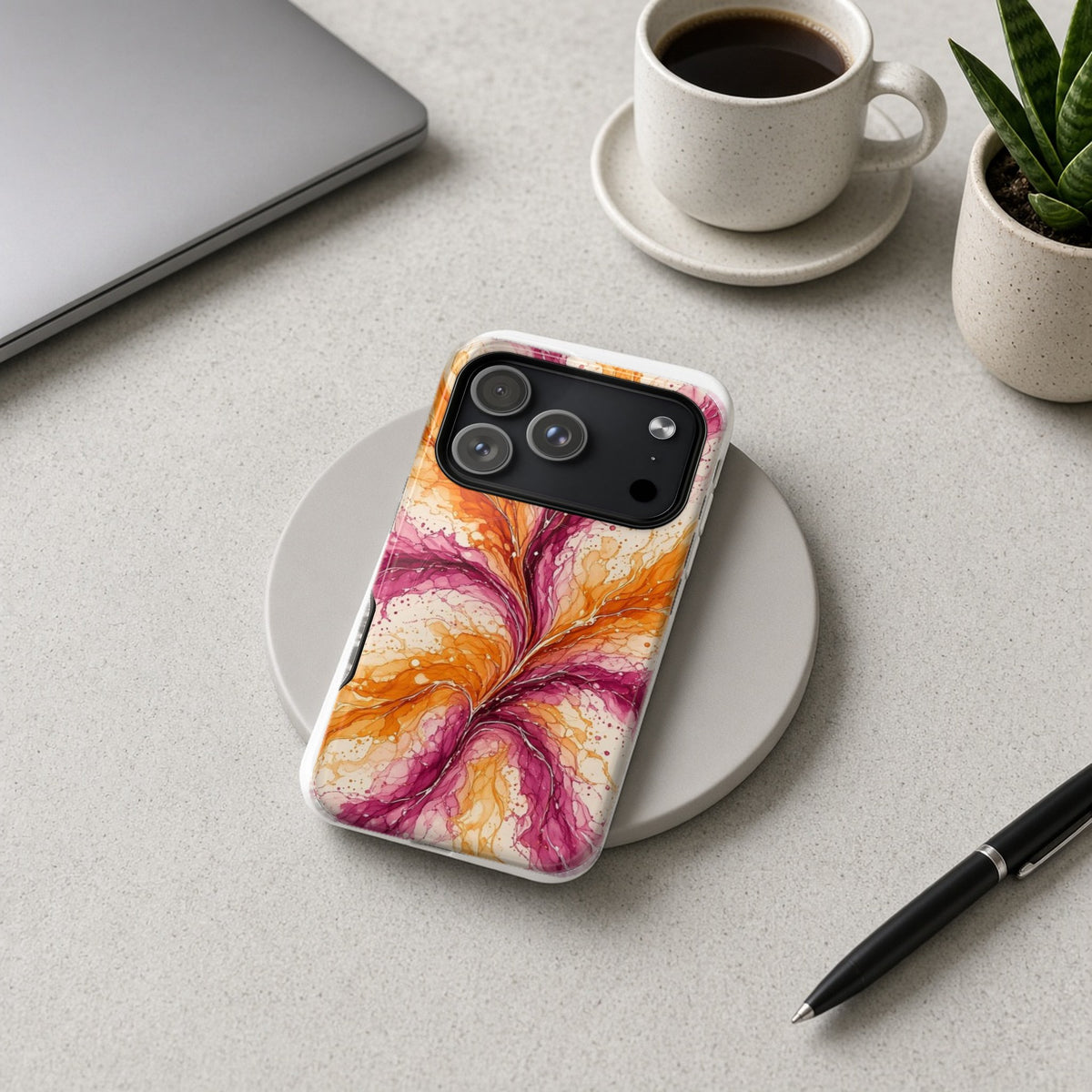 Sunset Ink Branches magnetic iPhone case on a wireless charging pad on a grey desk