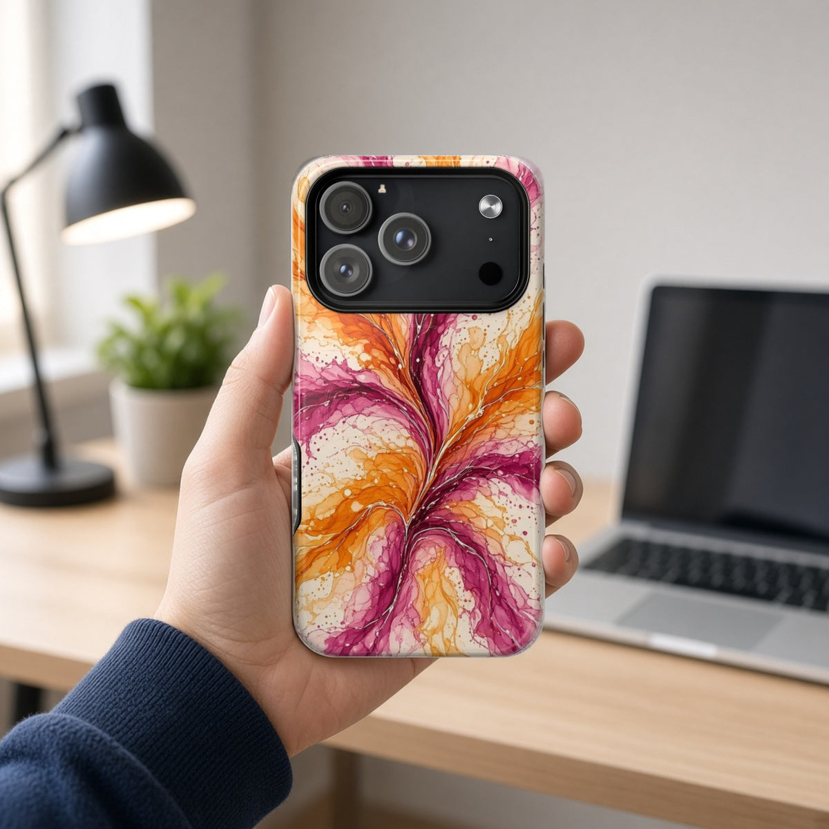 Hand holding the Sunset Ink Branches magnetic iPhone case at a home office desk