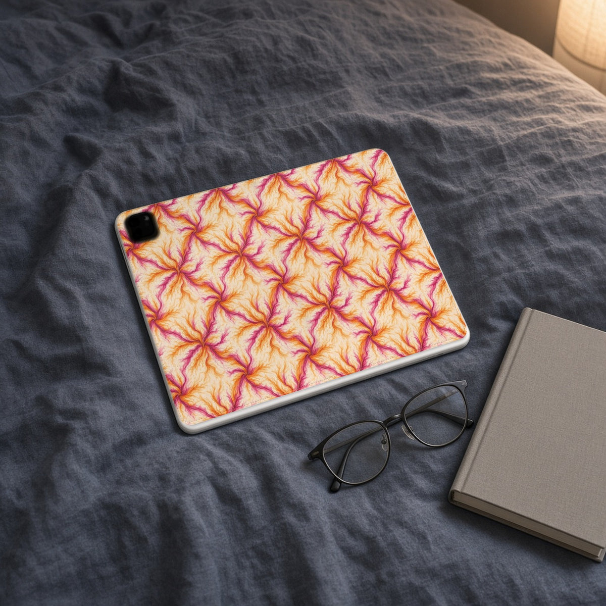 Sunset Ink Branches iPad folio case on slate-blue bedding with a book and glasses