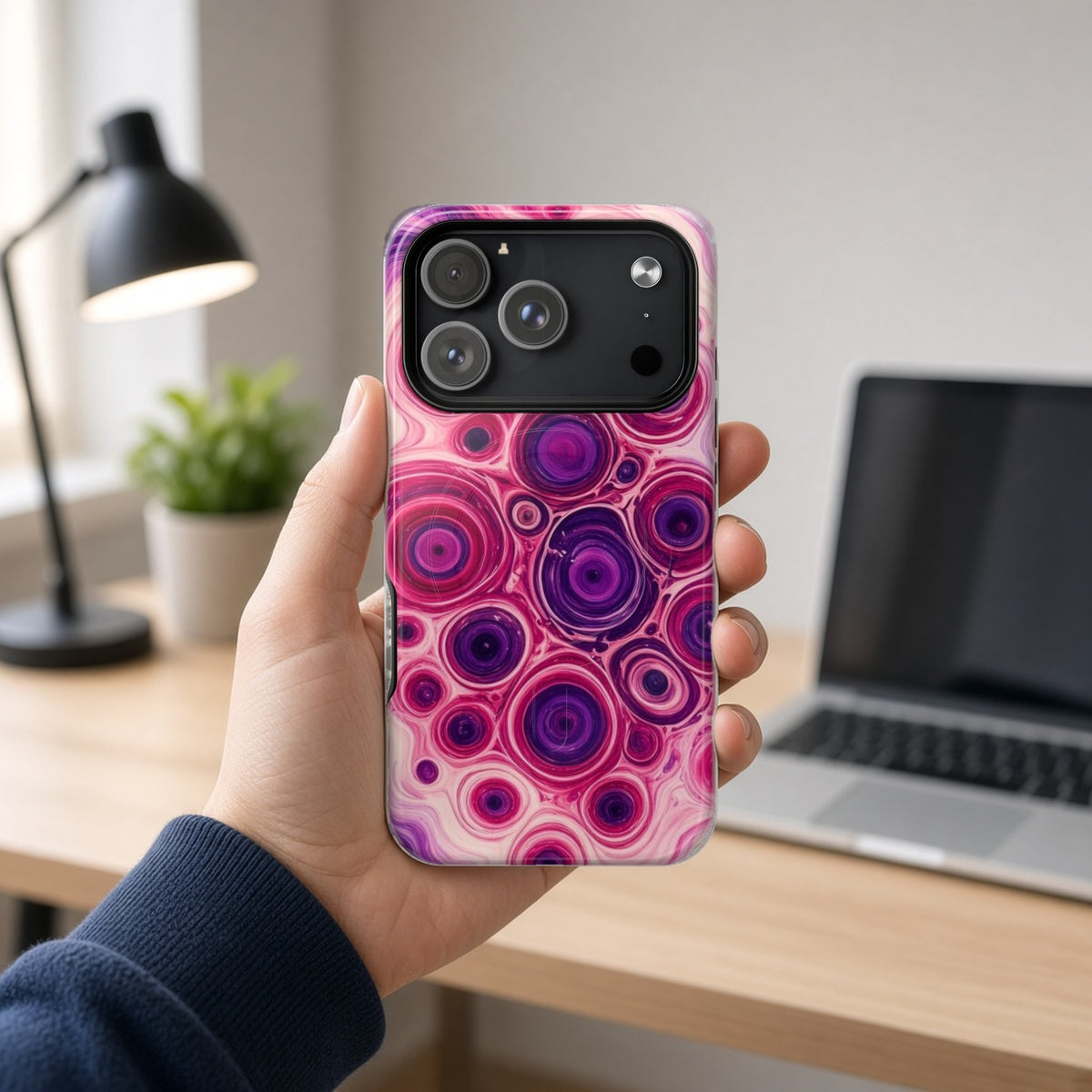 Hand holding the Berry Puddle Pour magnetic iPhone case at a home office desk