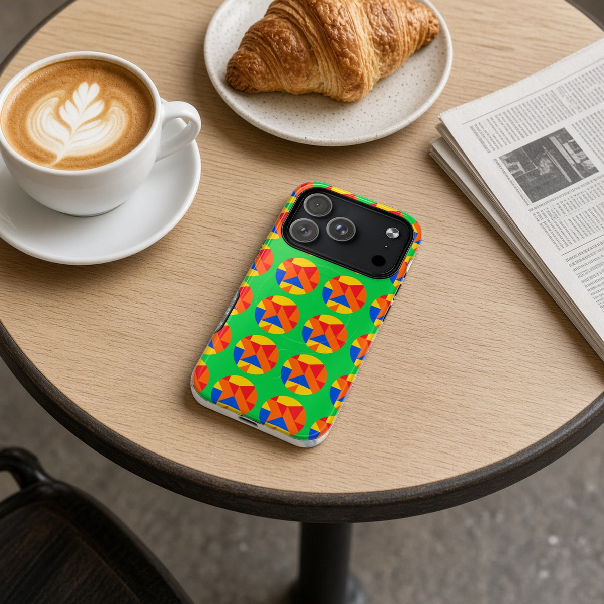 Broken Circle Planes magnetic iPhone case on a cafe table with a latte, croissant and newspaper