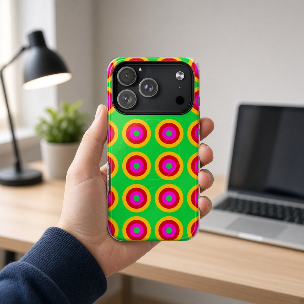 Hand holding the Giant Op-Art Jewel Rings magnetic iPhone case at a home office desk